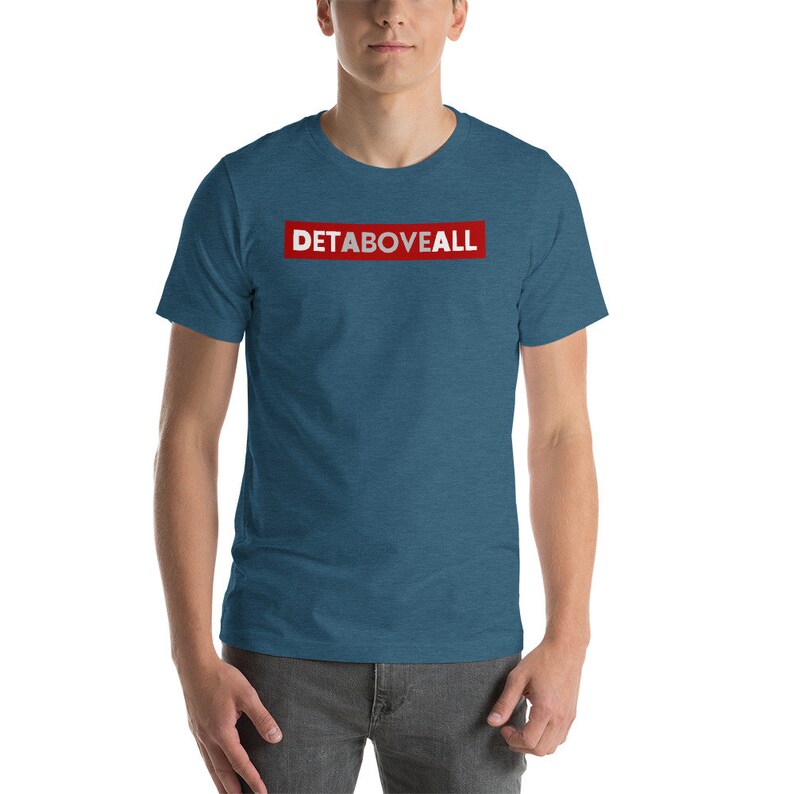 May include: Teal short-sleeved t-shirt with the text "DETABOVEALL" in white letters inside a red rectangle. The shirt is made of a soft, comfortable material.