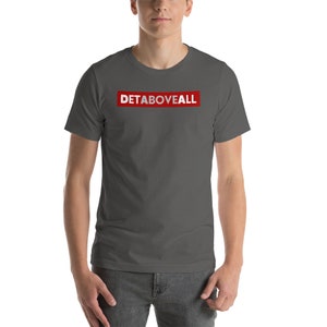 May include: A dark grey t-shirt featuring the text "DETABOVEALL" in white within a red rectangular box. The shirt has short sleeves and is likely made from a soft fabric.