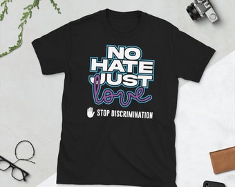 Może przedstawiać: Czarna koszulka z napisem "NO HATE JUST LOVE" w kolorze białym, niebieskim i fioletowym. Fraza "STOP DISCRIMINATION" jest wydrukowana pod symbolem dłoni. Widoczny jest aparat fotograficzny, okulary i portfel.