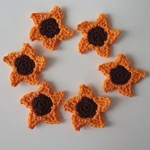 Könnte beinhalten: Sechs gehäkelte Sonnenblumen-Verzierungen in einem Kreis angeordnet. Die Sonnenblumen sind orange mit braunen Zentren.