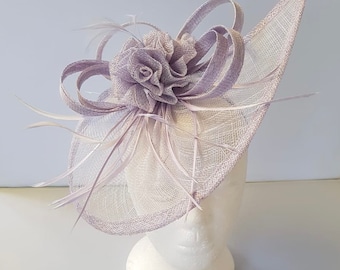 May include: A lavender-colored fascinator with a large flower and feathers. The fascinator is made of a delicate, netting material.