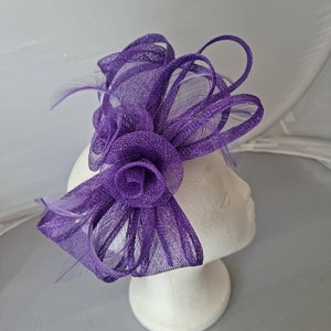 Könnte beinhalten: Eine lilafarbene Haarklammer mit einer Mesh-Blume und Federn. Die Blume besteht aus einem weichen, zarten Mesh-Gewebe und hat eine gekräuselte Optik. Die Federn sind weiß und verleihen der Klammer einen Hauch von Eleganz.