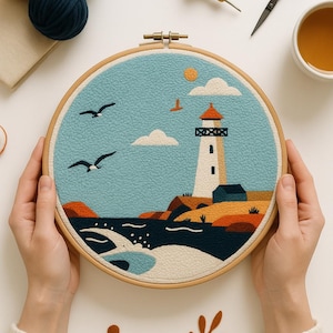 May include: A round embroidery hoop featuring a lighthouse scene with a blue sky, white clouds, and seagulls. The lighthouse is white with a red roof, set on a rocky shore. Crafting supplies, including yarn and scissors, are arranged around the hoop.