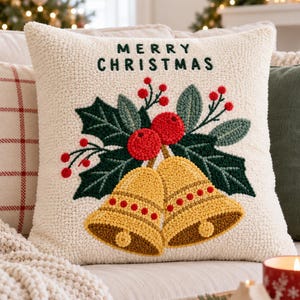 May include: A square cream-colored throw pillow featuring a textured punch needle design. The front displays the text MERRY CHRISTMAS in dark green, above a central motif of two yellow bells, dark green holly leaves, and bright red berries.