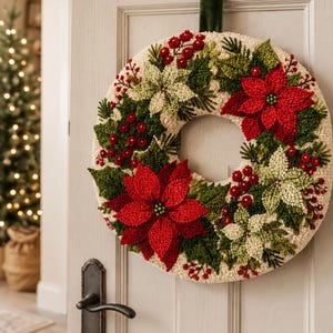 May include: A circular punch needle wreath featuring a cream-colored base decorated with red and pale green poinsettia flowers, dark green pine needles, and clusters of small red berries, suspended by a dark green velvet ribbon on a door.