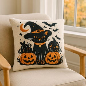 Puede incluir: Cojín decorativo de Halloween con un gato negro con sombrero de bruja, rodeado de calabazas talladas y murciélagos. El cojín tiene un fondo color crema y está sobre una silla beige.