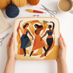 May include: A square embroidery hoop with a colorful abstract design of three dancing figures in shades of orange, blue, and black. The artwork is held by hands, with craft supplies like yarn, scissors, and a cup of coffee in the background.