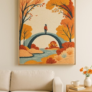 May include: Framed artwork depicting a person standing on a bridge in a fall landscape. The scene features a river, trees with orange and yellow foliage, and a beige background. The artwork is in a wooden frame.