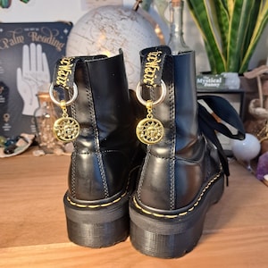 May include: Black leather platform boots with yellow stitching and gold charms. The charms are round and feature a sun design.
