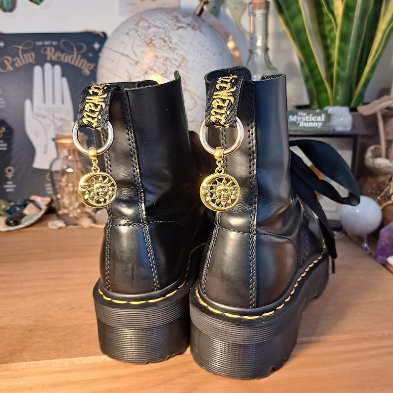 May include: Black leather platform boots with yellow stitching and gold charms. The charms are round and feature a sun design.