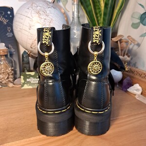 May include: Black leather platform boots with yellow stitching and gold charms. The charms feature a sun and moon design with the text "Mystic Sun" on the straps.