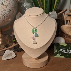 May include: A silver chain necklace with a pendant featuring three pastel-coloured flower charms and green leaves.