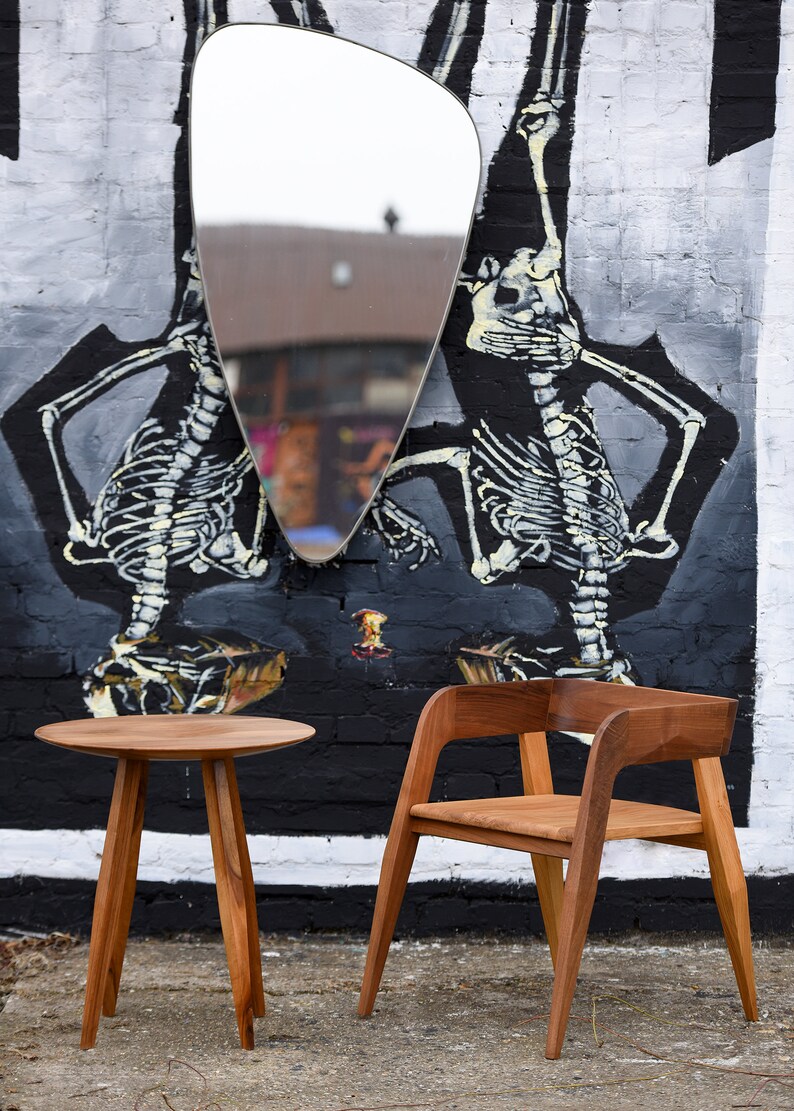 May include: A wooden table and chair set against a brick wall with a large, abstract mural of skeletons. The table has a round top and three legs, while the chair has a curved back and four legs.