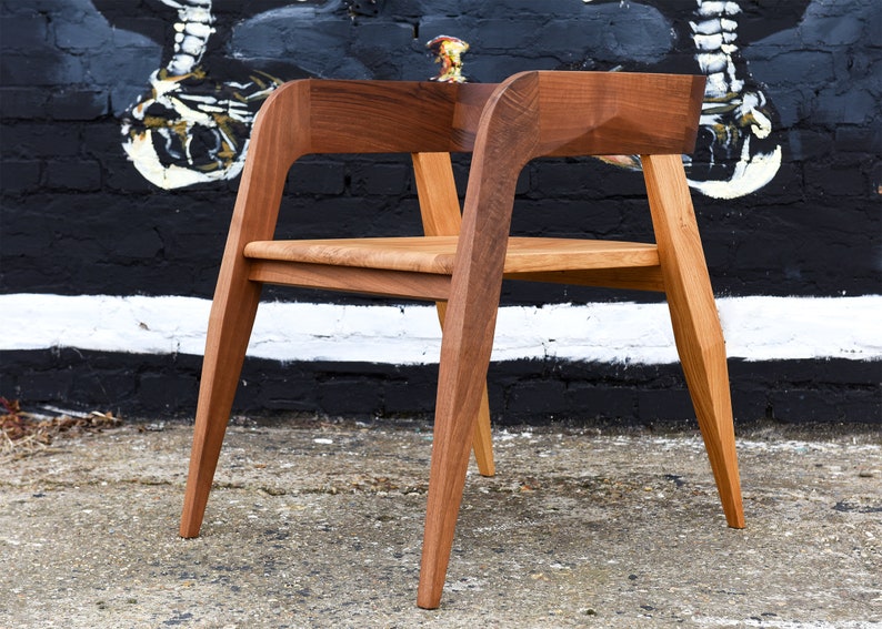 May include: A wooden chair with a unique design. The chair has a curved back and angled legs. The chair is made of light brown wood.
