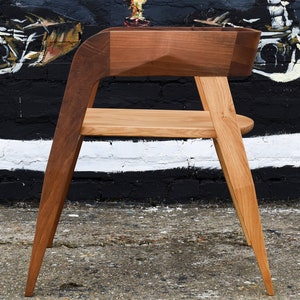 May include: A wooden chair with a unique design. The chair has a curved back and a wide seat. The legs are angled and the chair is made of two different types of wood.