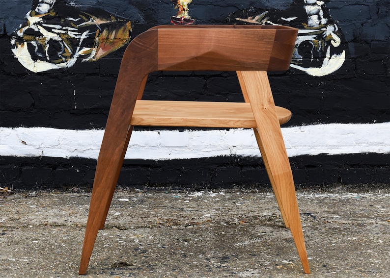 May include: A wooden chair with a unique design. The chair has a curved back and a wide seat. The legs are angled and the chair is made of two different types of wood.