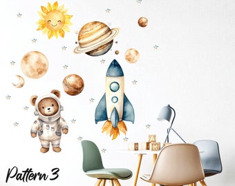 May include: A set of space-themed wall decals featuring a rocket, planets, stars, a sun, and a bear wearing an astronaut suit. The decals are shown on a white wall in a room with furniture.