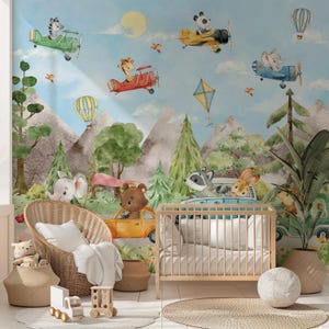 May include: A nursery wall mural with a watercolor design featuring animals in hot air balloons and airplanes. The mural features a raccoon, a rabbit, a giraffe, a panda, a zebra, and a squirrel. The mural is set against a blue sky with white clouds.