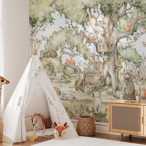 Op de afbeelding: Een witte tipi-tent met een witte pompon-bies staat in een kamer met een bosmuurschildering met een grote boom met een boomhut, dieren en een blauwe lucht.