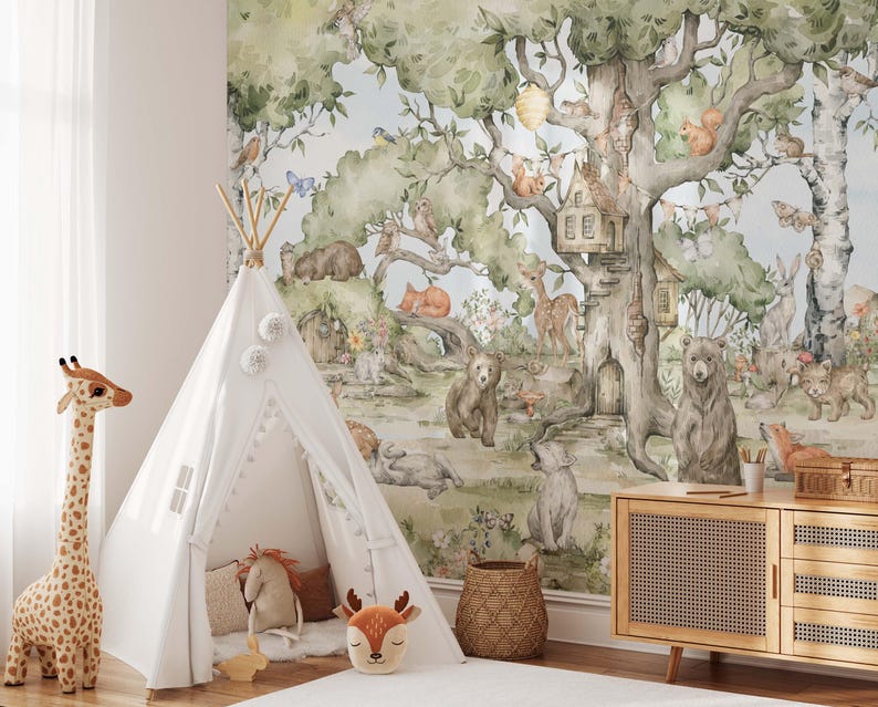 Op de afbeelding: Een witte tipi-tent met een witte pompon-bies staat in een kamer met een bosmuurschildering met een grote boom met een boomhut, dieren en een blauwe lucht.
