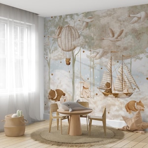 Op de afbeelding: Een grillige kinderkamersc&egrave;ne met een muurschildering met een heteluchtballon, zwanen en een zeilboot. De kamer bevat een ronde houten tafel, stoelen en een gevlochten mand. Een pluche walvis en een stervormig kussen dragen bij aan de inrichting.
