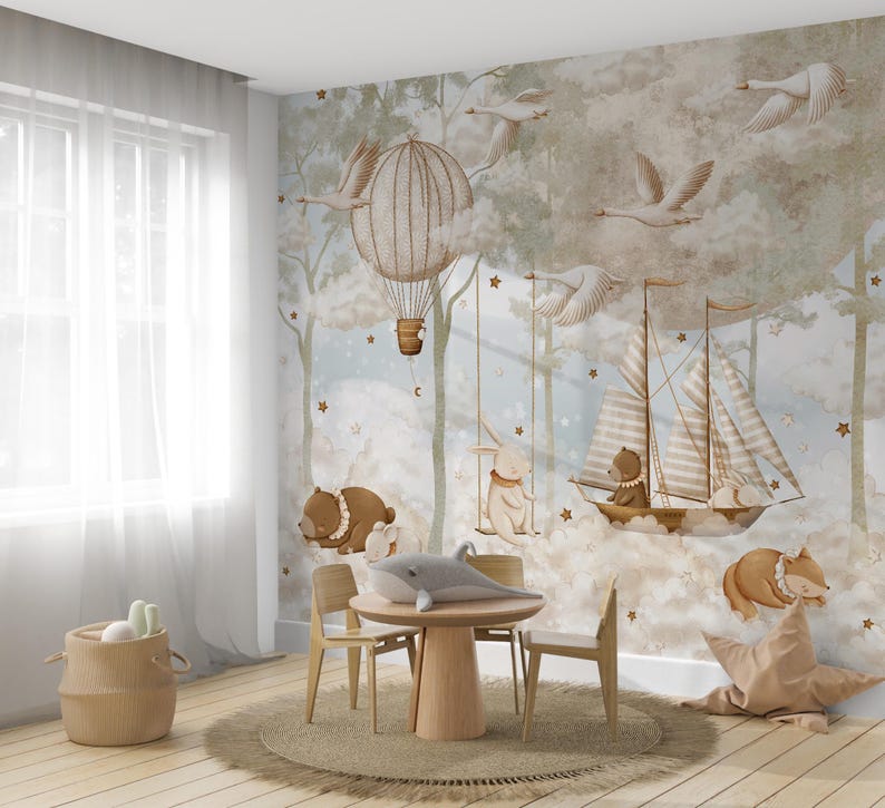 Op de afbeelding: Een grillige kinderkamersc&egrave;ne met een muurschildering met een heteluchtballon, zwanen en een zeilboot. De kamer bevat een ronde houten tafel, stoelen en een gevlochten mand. Een pluche walvis en een stervormig kussen dragen bij aan de inrichting.