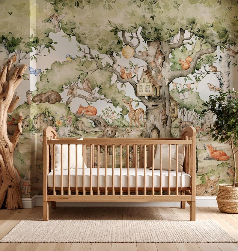 Puede incluir: Una cuna de madera con un colch&oacute;n blanco se encuentra frente a un mural caprichoso con tem&aacute;tica de bosque. El mural presenta ilustraciones de acuarela de criaturas del bosque, &aacute;rboles y una casa de hadas.