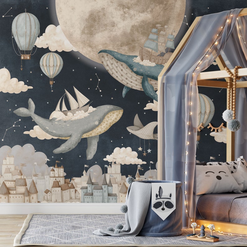 May include: A whimsical nursery wall mural featuring a dark blue background with clouds, stars, and a large moon. Two blue whales are flying through the sky, one carrying a sailboat and the other a ship. A small town with buildings is at the bottom of the mural.
