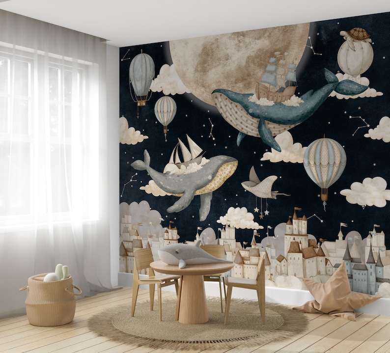 May include: A whimsical nursery wall mural featuring a dark blue night sky with white stars, clouds, and a large, full moon. Two blue whales fly through the sky with hot air balloons and ships. The mural also features a cityscape of white buildings with brown roofs.