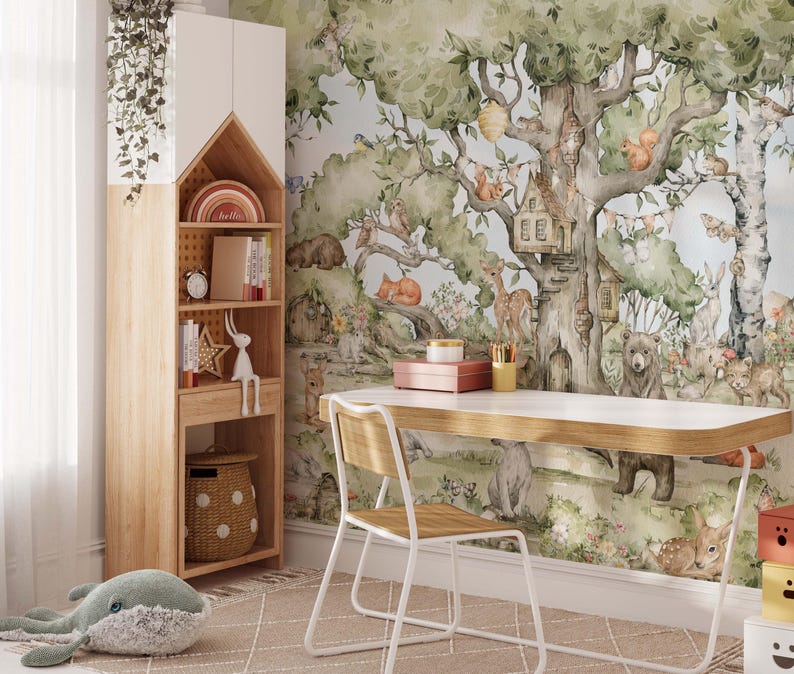 Op de afbeelding: Een wit bureau met een houten blad staat voor een muurschildering die een fantasierijk boslandschap voorstelt met een boomhut, dieren en bladeren. De muurschildering is geschilderd in aquarelstijl met tinten groen, bruin en blauw. Een witte stoel met een houten zitting staat naast het bureau.