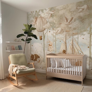 Op de afbeelding: Een kinderkamer met een licht houten wieg, een schommelstoel en een grillige muurschildering met luchtballonnen, zwanen en bosdieren. De kamer heeft een neutraal kleurenpalet met een beige tapijt en een groene plant.