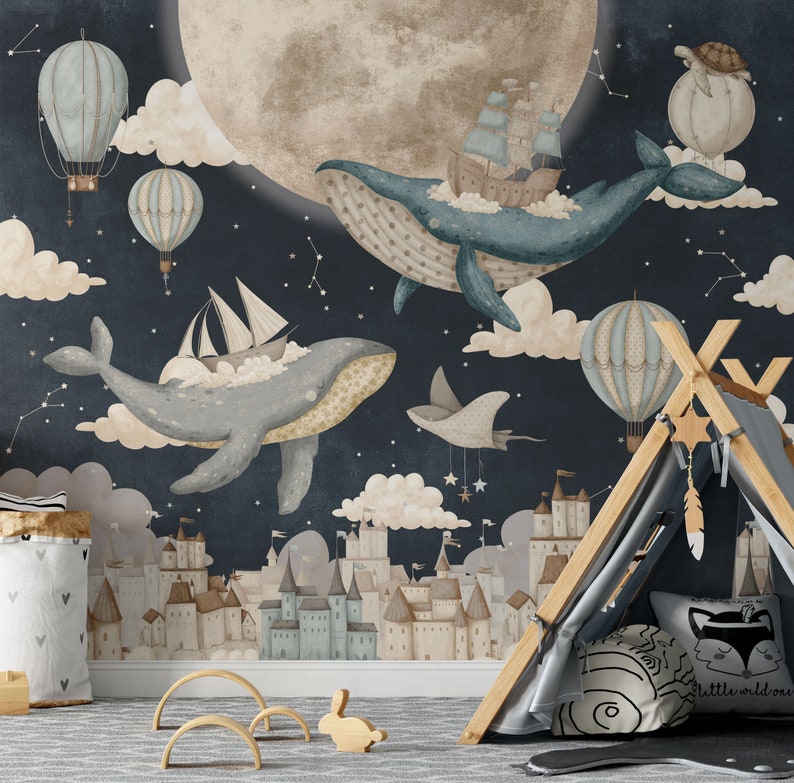 May include: A whimsical nursery wall mural featuring two blue whales flying through a starry night sky with clouds, a moon, and hot air balloons. The whales are carrying ships and a small flying creature. The mural also features a small town with castle-like buildings.