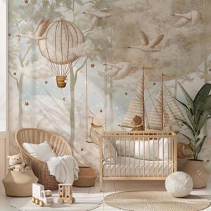 Op de afbeelding: Een kinderkamer met een muurschildering van een luchtballon, zwanen en een konijn op een schommel. De kamer omvat een houten wieg, een rieten stoel en geweven manden, allemaal in een zacht, neutraal kleurenpalet.