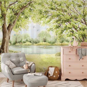 May include: A nursery scene featuring a watercolor mural of a serene lakeside landscape with trees and butterflies. A gray armchair and ottoman, a pink dresser, and a woven basket complete the room's decor.