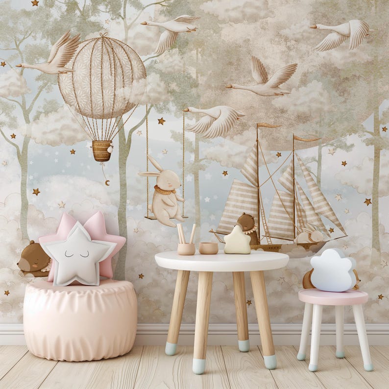 Op de afbeelding: Een grillige kinderkamersc&egrave;ne met een lichtblauwe en beige muurschildering met een luchtballon, zwanen en een zeilboot. De kamer heeft een roze poef, stervormige kussens, een kleine tafel en een kruk. Een konijn schommelt.