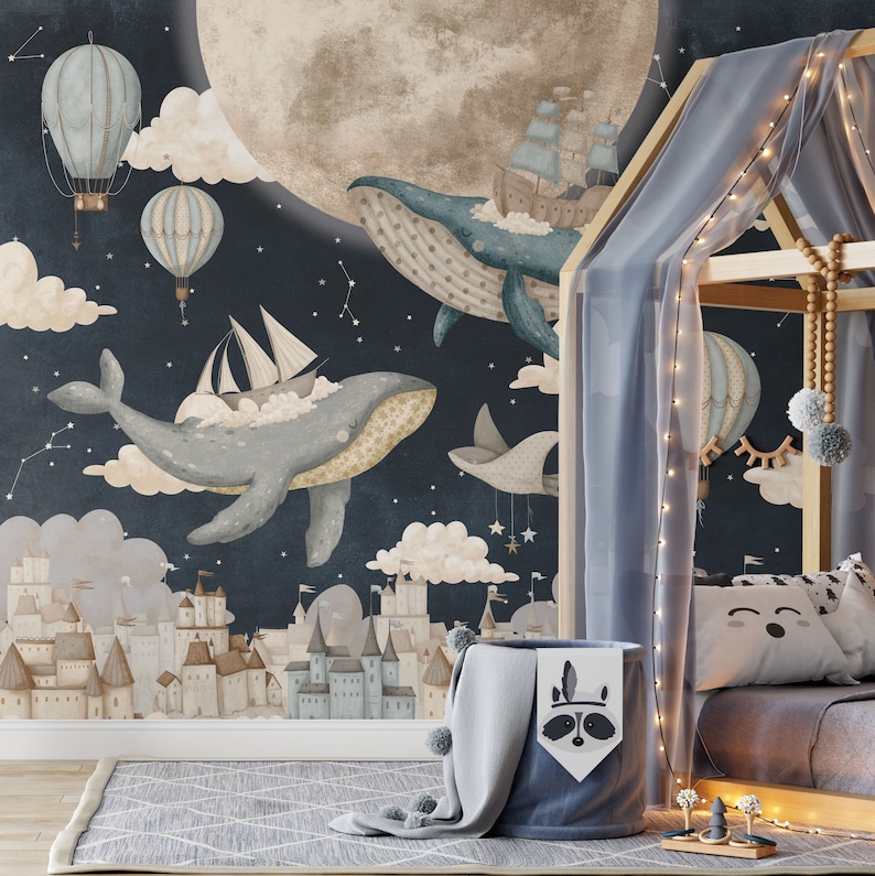 May include: A whimsical nursery wall mural featuring a dark blue background with white clouds, stars, and a large moon. Two blue whales are flying through the sky, one carrying a sailboat and the other carrying a ship. A small town with buildings is at the bottom of the mural.