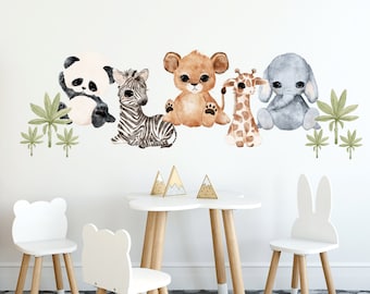 May include: Watercolor wall decals featuring a panda, zebra, lion cub, giraffe, and elephant. The nursery decor includes green palm leaves and is set above a white table and chairs. The room has a gray rug and wooden accents.
