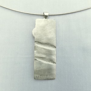 May include: Silver pendant with a textured surface and the number 925 stamped on the back.
