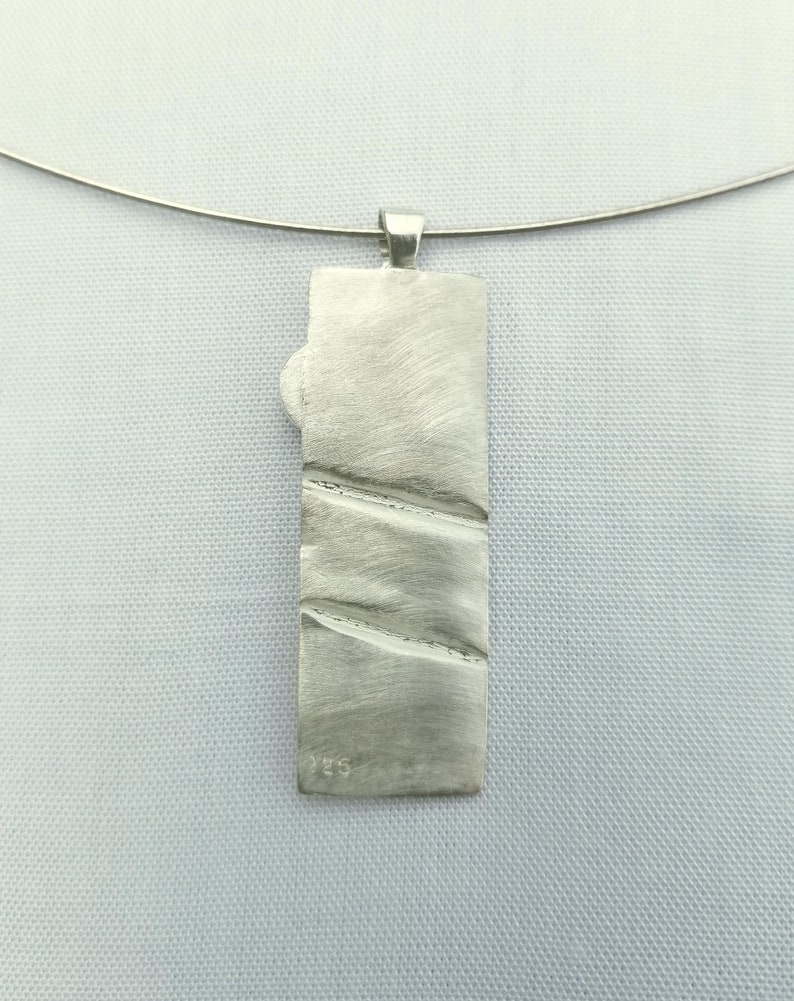 May include: Silver pendant with a textured surface and the number 925 stamped on the back.