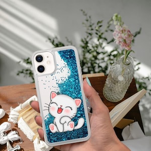 Könnte beinhalten: Eine transparente Handyhülle mit blauem Glitzerhintergrund und einer weißen Comic-Katze mit rosa Nase und Mund. Die Katze lächelt und hat ihre Pfoten in der Luft.