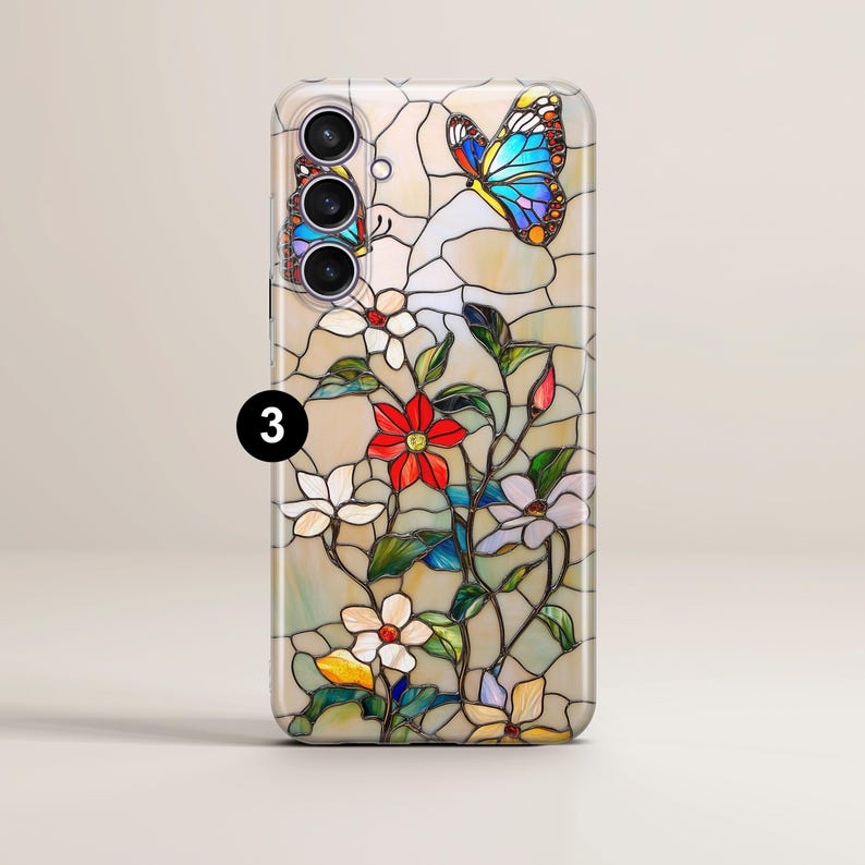 May include: A phone case featuring a stained-glass design with a butterfly and floral motif. The case has a cream-colored background with a colorful butterfly and flowers in red, white, and yellow. The number "3" is visible.