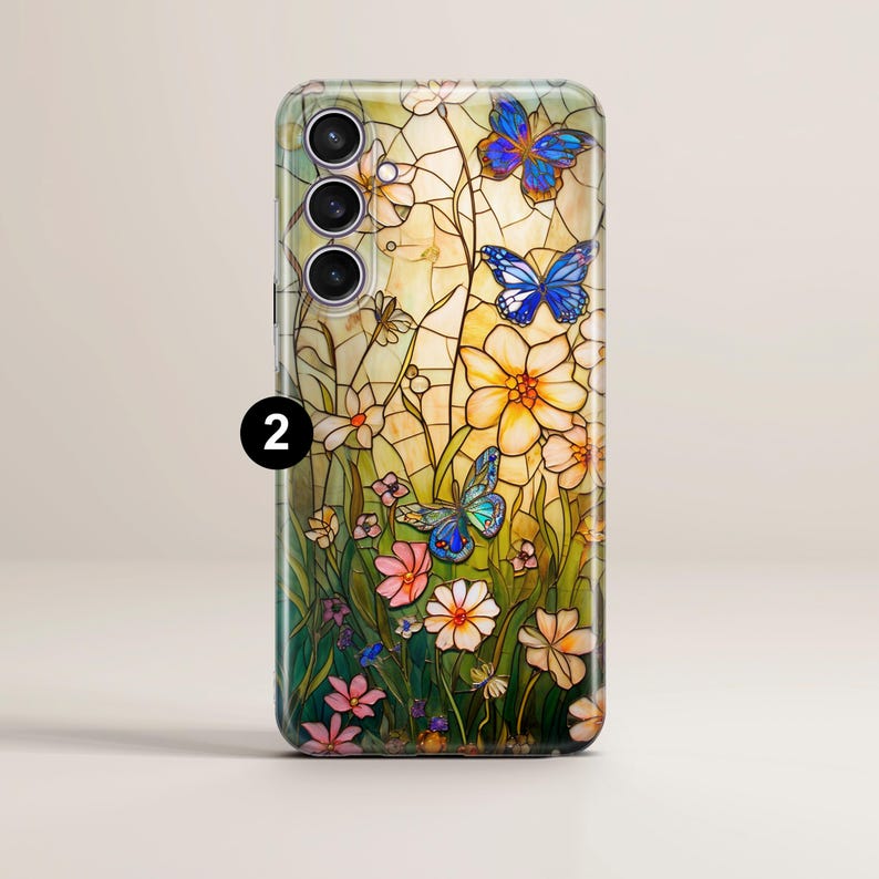 May include: A phone case featuring a stained-glass design with butterflies and flowers. The case has a colorful, artistic design with blue butterflies, white and yellow flowers, and green grass. The case has a glossy finish and a camera cutout.
