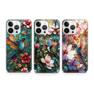 May include: Three iPhone cases with a stained glass design featuring colorful hummingbirds and flowers. The cases are clear and show the phone's design through the case.