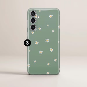 May include: A green phone case with a daisy pattern. The case has a matte finish and features small white daisies with yellow centers scattered across the surface. The phone case has three camera lenses and a flash.