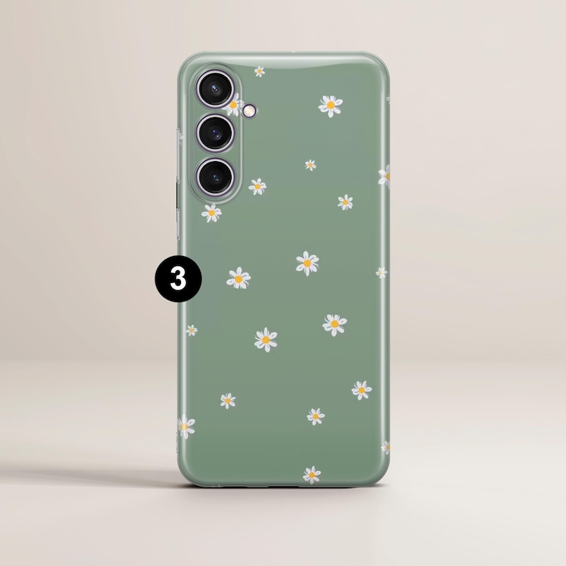 May include: A green phone case with a daisy pattern. The case has a matte finish and features small white daisies with yellow centers scattered across the surface. The phone case has three camera lenses and a flash.