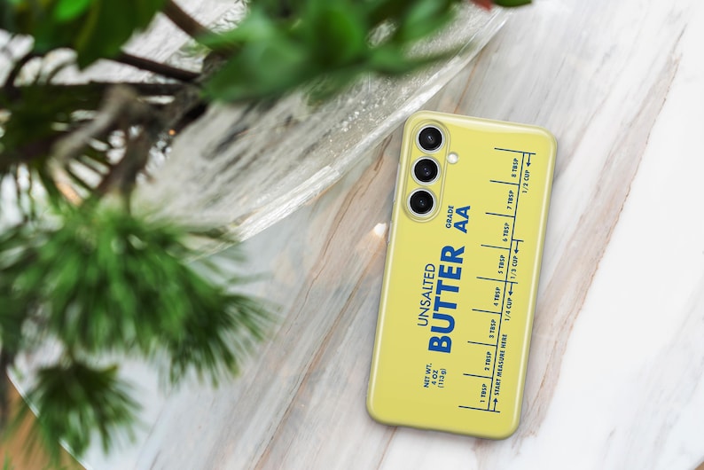 May include: A yellow phone case with a stick of butter design. The case has a blue label that reads "Unsalted Butter AA Grade" and a measurement guide in tablespoons and cups.