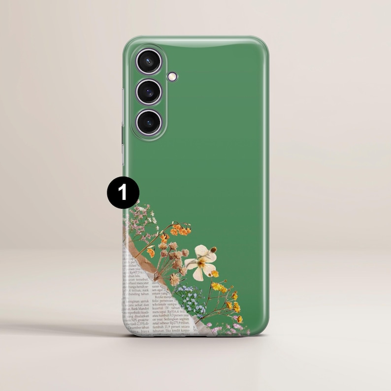 May include: A green phone case with a floral design. The case features a glossy finish and a camera module on the upper left. The floral design includes white, yellow, and blue flowers, with a section of newspaper print.