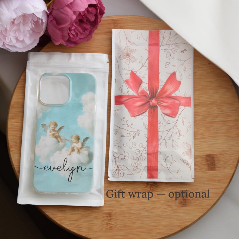May include: A light blue phone case featuring cherubs on clouds, with the name "evelyn" in script. The case is in a clear plastic sleeve, next to a gift bag with a red bow and floral pattern. Pink flowers are in the background.