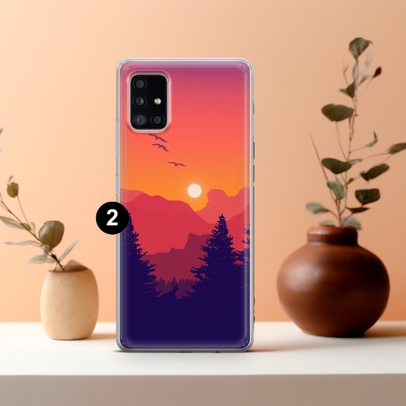 May include: A clear phone case with a sunset scene over mountains and trees. The case has a purple, orange, and pink gradient background with a silhouette of trees and mountains. The sun is setting in the distance.
