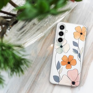 May include: Clear phone case with a floral design. The case features orange, pink, and light green flowers with gray leaves. The phone case has a camera cutout with three lenses.